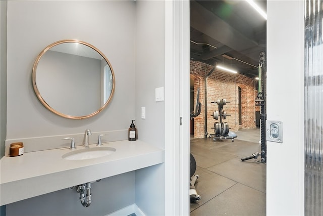 bathroom with brick wall, concrete floors, and a sink