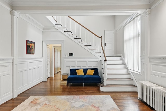 stairway featuring ornamental molding, a wainscoted wall, radiator, a decorative wall, and wood finished floors