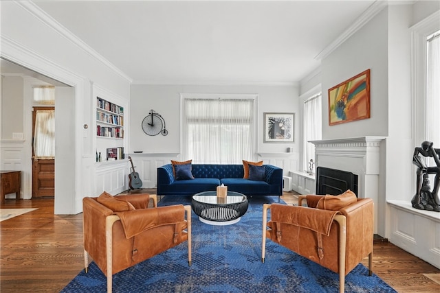 living area featuring crown molding, built in shelves, wood finished floors, and a fireplace