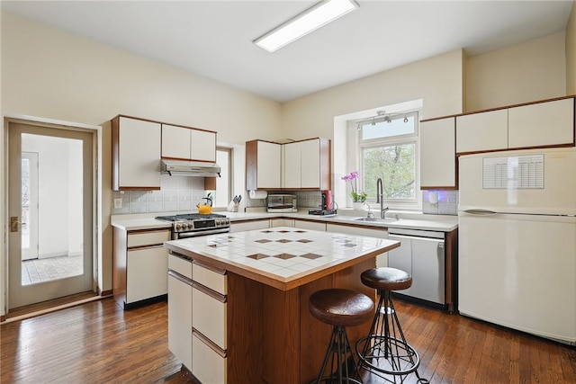 kitchen featuring tile counters, a kitchen island, under cabinet range hood, stainless steel appliances, and a sink