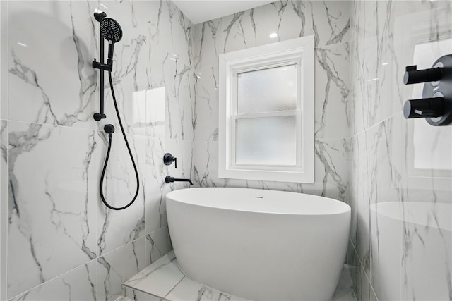 bathroom featuring marble finish floor, a soaking tub, stone wall, and a marble finish shower