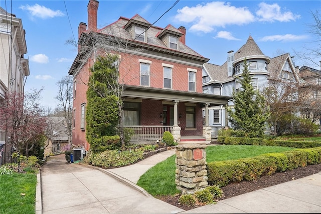 view of front of home featuring a chimney, cooling unit, a front lawn, a porch, and brick siding
