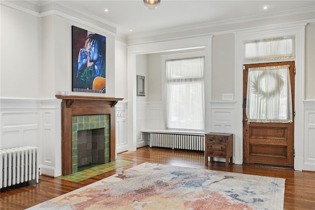 entrance foyer with radiator, wood finished floors, a fireplace, and ornamental molding
