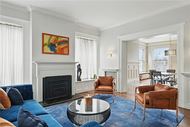living room featuring crown molding, a fireplace with raised hearth, and wood finished floors