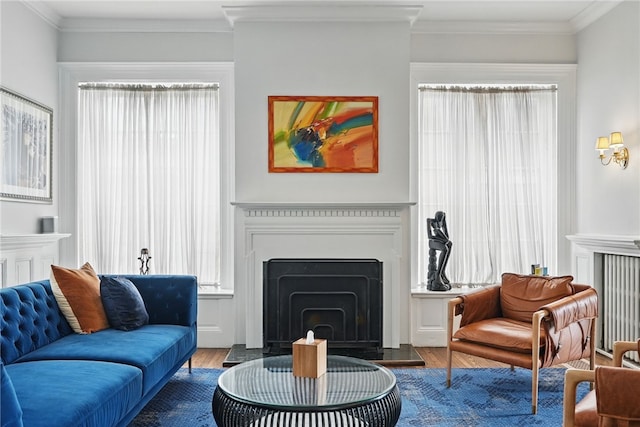living area with a healthy amount of sunlight, a fireplace with raised hearth, crown molding, and wood finished floors