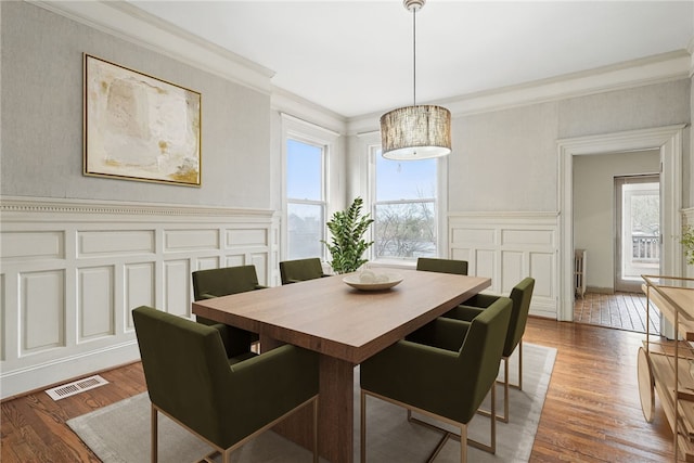 dining space with ornamental molding, visible vents, a decorative wall, and wood finished floors