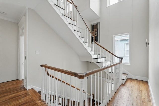 stairway featuring baseboards, a towering ceiling, and hardwood / wood-style flooring