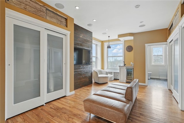 living area featuring wine cooler, baseboards, light wood finished floors, and radiator
