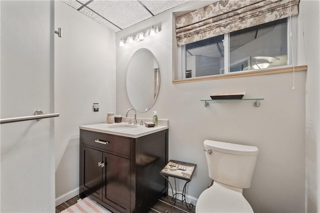 bathroom with toilet, vanity, baseboards, and a drop ceiling