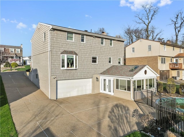 rear view of property featuring fence, brick siding, an attached garage, french doors, and driveway