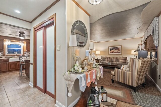 hallway featuring baseboards, a sink, crown molding, and light tile patterned flooring