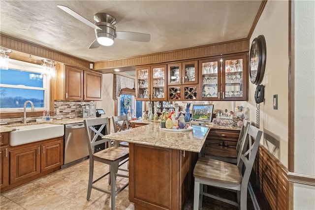 kitchen with a sink, brown cabinetry, stainless steel dishwasher, and a breakfast bar