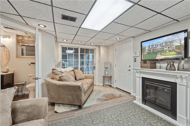 living area featuring visible vents, recessed lighting, a drop ceiling, and a glass covered fireplace