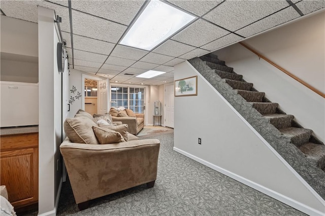 living area with baseboards, a drop ceiling, and stairs