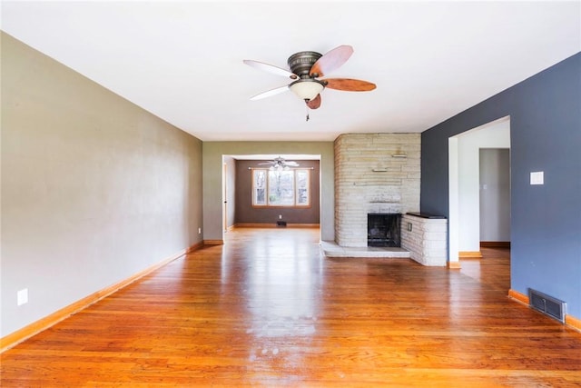 unfurnished living room featuring visible vents, baseboards, a stone fireplace, ceiling fan, and light wood-type flooring