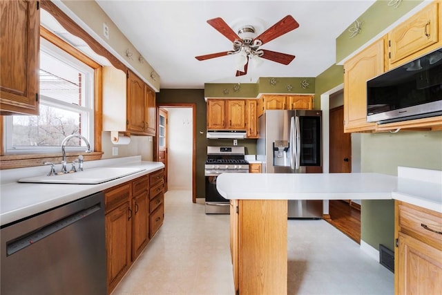 kitchen featuring a sink, light countertops, appliances with stainless steel finishes, a ceiling fan, and under cabinet range hood