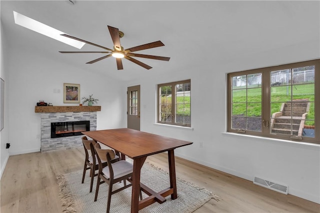 dining space featuring baseboards, a fireplace, visible vents, ceiling fan, and light wood finished floors