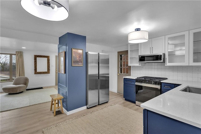 kitchen featuring tasteful backsplash, light wood-style floors, white cabinetry, stainless steel appliances, and blue cabinetry