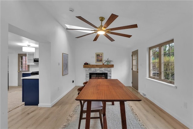 dining space featuring visible vents, ceiling fan, a fireplace, light wood finished floors, and vaulted ceiling
