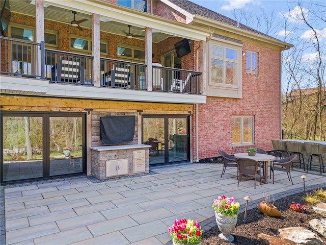 back of property featuring brick siding, outdoor dining space, a balcony, and a patio area