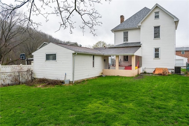 back of house with fence, a shingled roof, a lawn, and a chimney