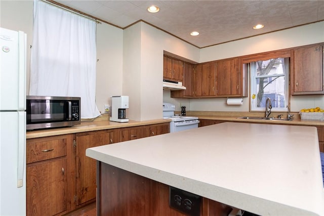 kitchen with a sink, light countertops, white appliances, under cabinet range hood, and brown cabinets