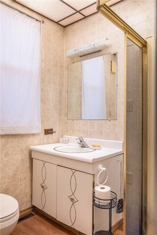bathroom featuring vanity, visible vents, toilet, wood finished floors, and tile walls