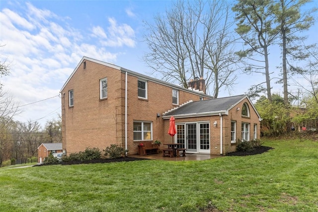 back of property featuring brick siding, a patio area, a yard, and a chimney