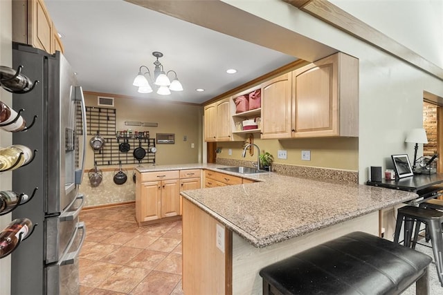 kitchen featuring light brown cabinetry, a sink, freestanding refrigerator, a peninsula, and a chandelier