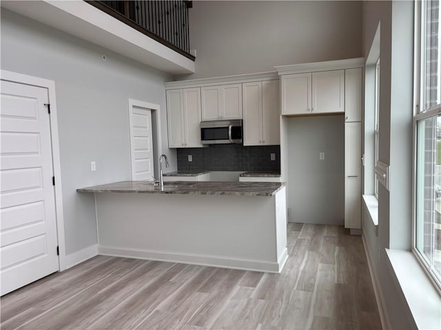 kitchen featuring tasteful backsplash, a high ceiling, stainless steel microwave, light wood finished floors, and stone countertops