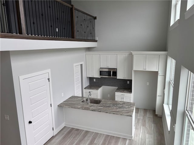 kitchen with a towering ceiling, white cabinetry, stone countertops, stainless steel microwave, and a sink