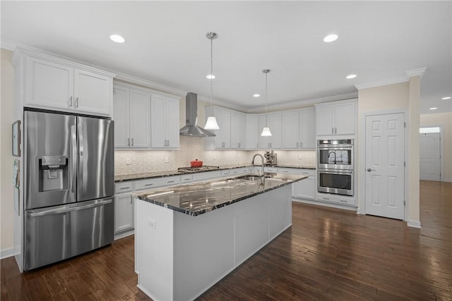 kitchen featuring wall chimney range hood, tasteful backsplash, white cabinets, a sink, and appliances with stainless steel finishes