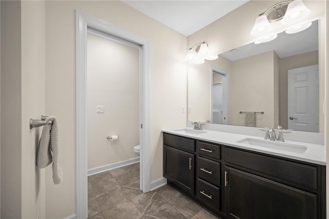 bathroom featuring baseboards, toilet, double vanity, and a sink