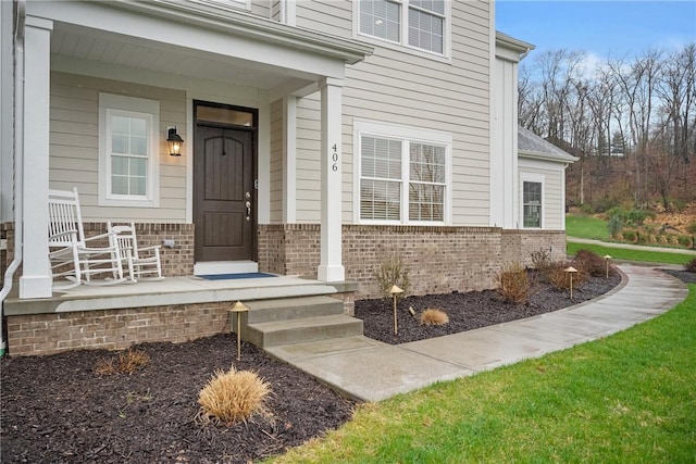 entrance to property featuring covered porch and brick siding