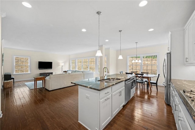 kitchen featuring an island with sink, dark stone counters, appliances with stainless steel finishes, a sink, and white cabinetry