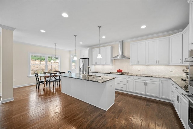 kitchen with dark stone counters, a sink, stainless steel appliances, wall chimney exhaust hood, and backsplash