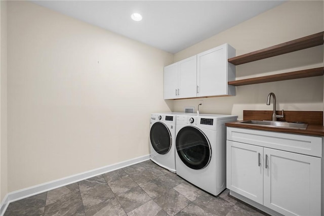 clothes washing area with separate washer and dryer, cabinet space, stone finish flooring, a sink, and baseboards