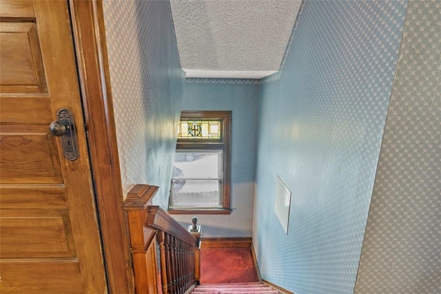 stairs with a textured ceiling, wallpapered walls, and carpet