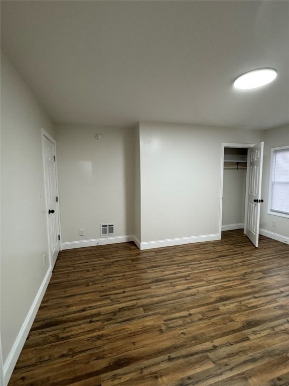 unfurnished bedroom with dark wood-style flooring, visible vents, a closet, and baseboards