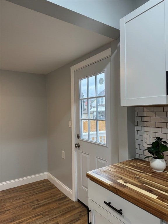 doorway featuring baseboards and dark wood-type flooring