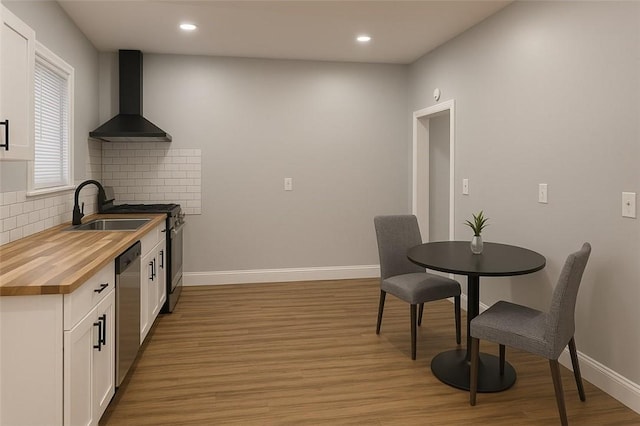 kitchen featuring a sink, decorative backsplash, wall chimney range hood, stainless steel dishwasher, and butcher block counters