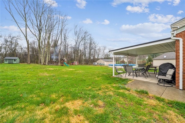 view of yard featuring an outbuilding, a patio area, a playground, and a storage unit