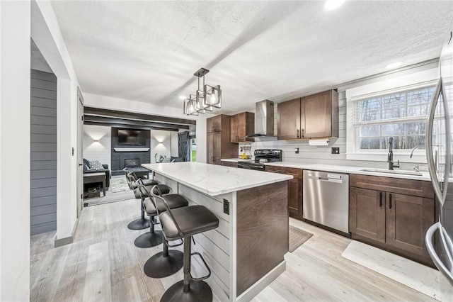 kitchen with wall chimney exhaust hood, light wood-type flooring, a center island, a sink, and stainless steel appliances