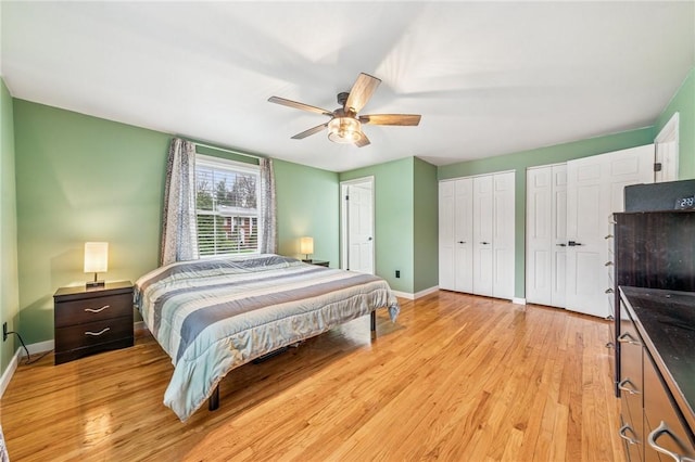 bedroom with light wood-type flooring, ceiling fan, baseboards, and two closets