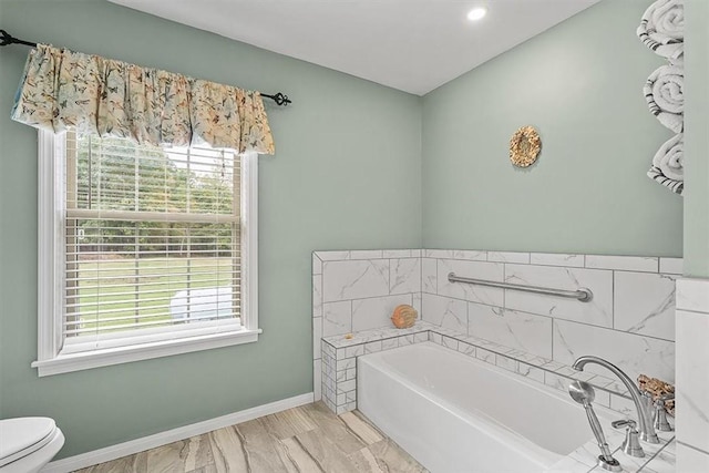 bathroom featuring toilet, a garden tub, baseboards, and a healthy amount of sunlight