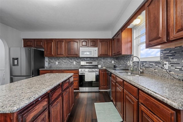 kitchen featuring arched walkways, a sink, dark wood finished floors, light stone countertops, and stainless steel appliances