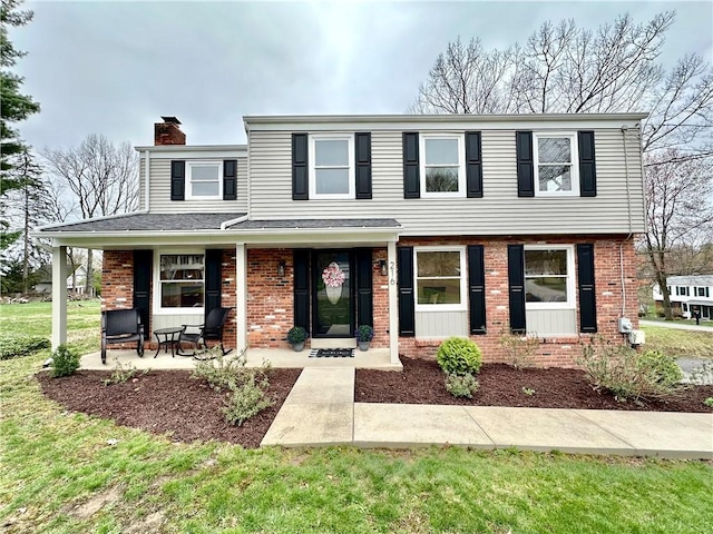 view of front facade featuring brick siding, a front yard, covered porch, and a chimney