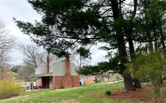 view of side of home featuring a chimney, brick siding, a patio area, and a yard