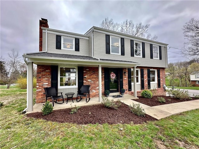 view of front of home with brick siding, a front yard, a porch, and a chimney