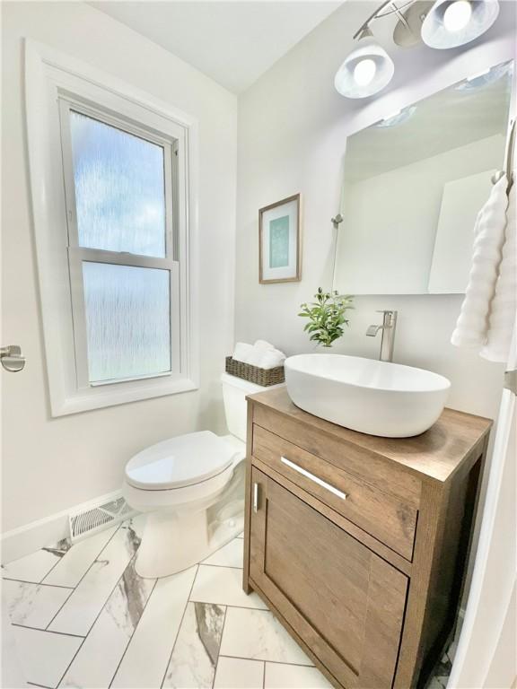 bathroom with vanity, visible vents, toilet, marble finish floor, and baseboards